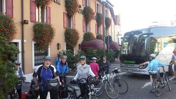 En gruppe cyklister og en bus foran en bygning med røde skodder og blomsterkasser.