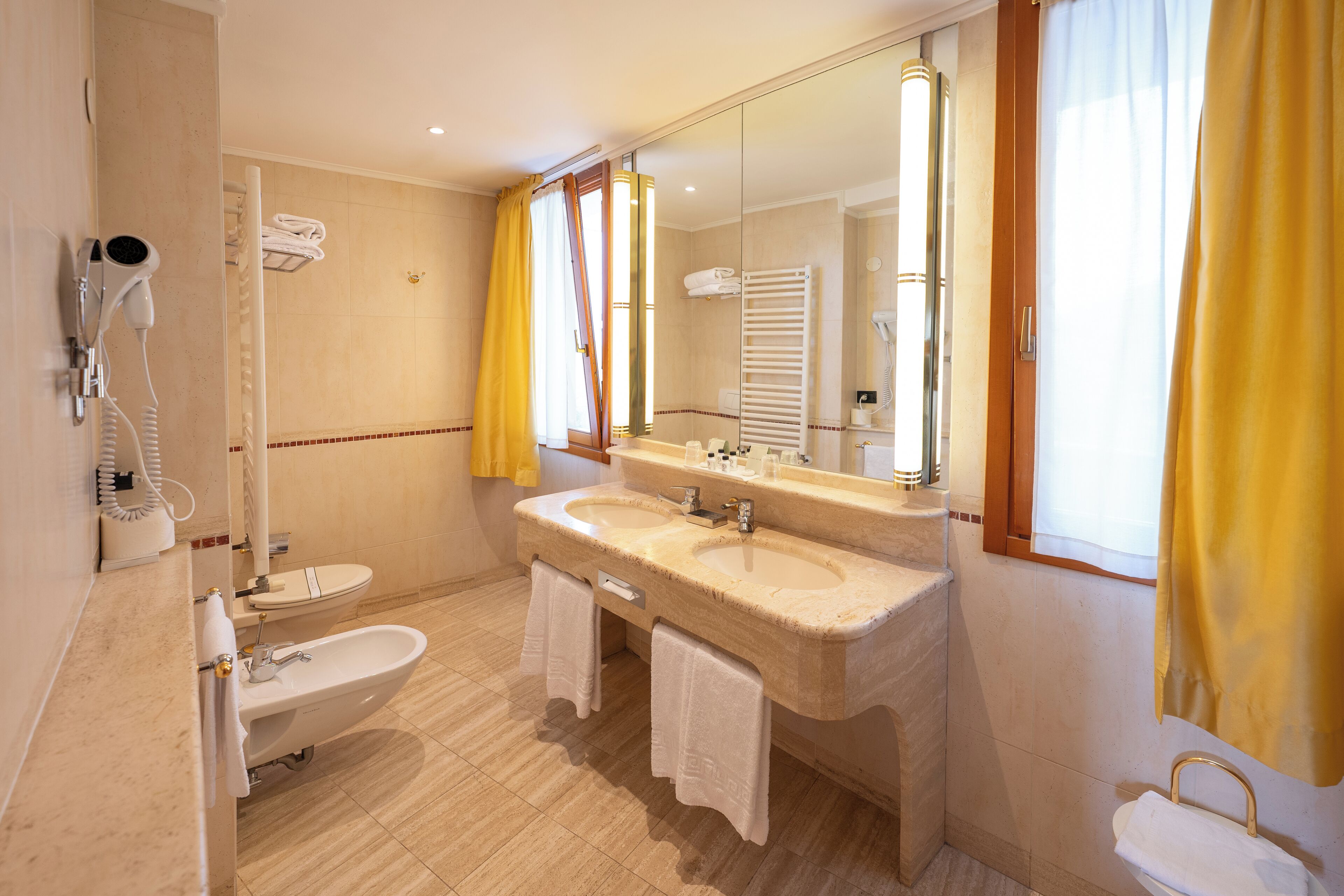 A bathroom with a double sink, a bathtub, a hairdryer, and a mirror.