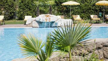 A swimming pool with lounge chairs and umbrellas, surrounded by greenery.