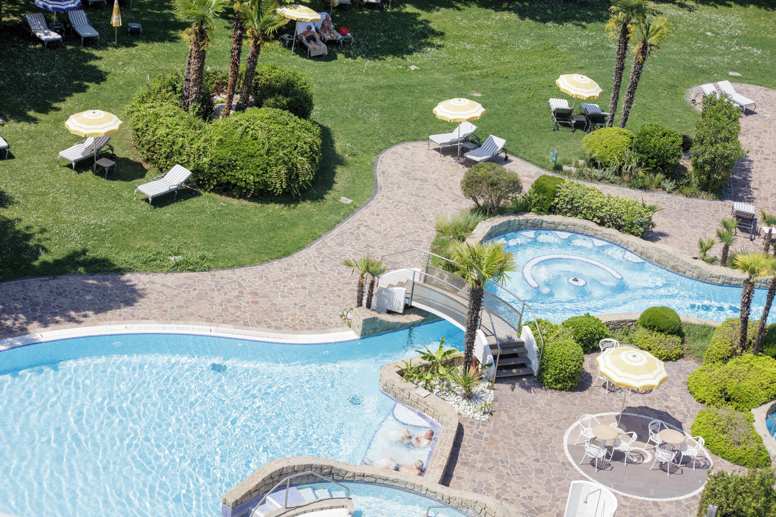 Eine Luftaufnahme eines Resorts mit einem großen Swimmingpool, Liegestühlen und Palmen.