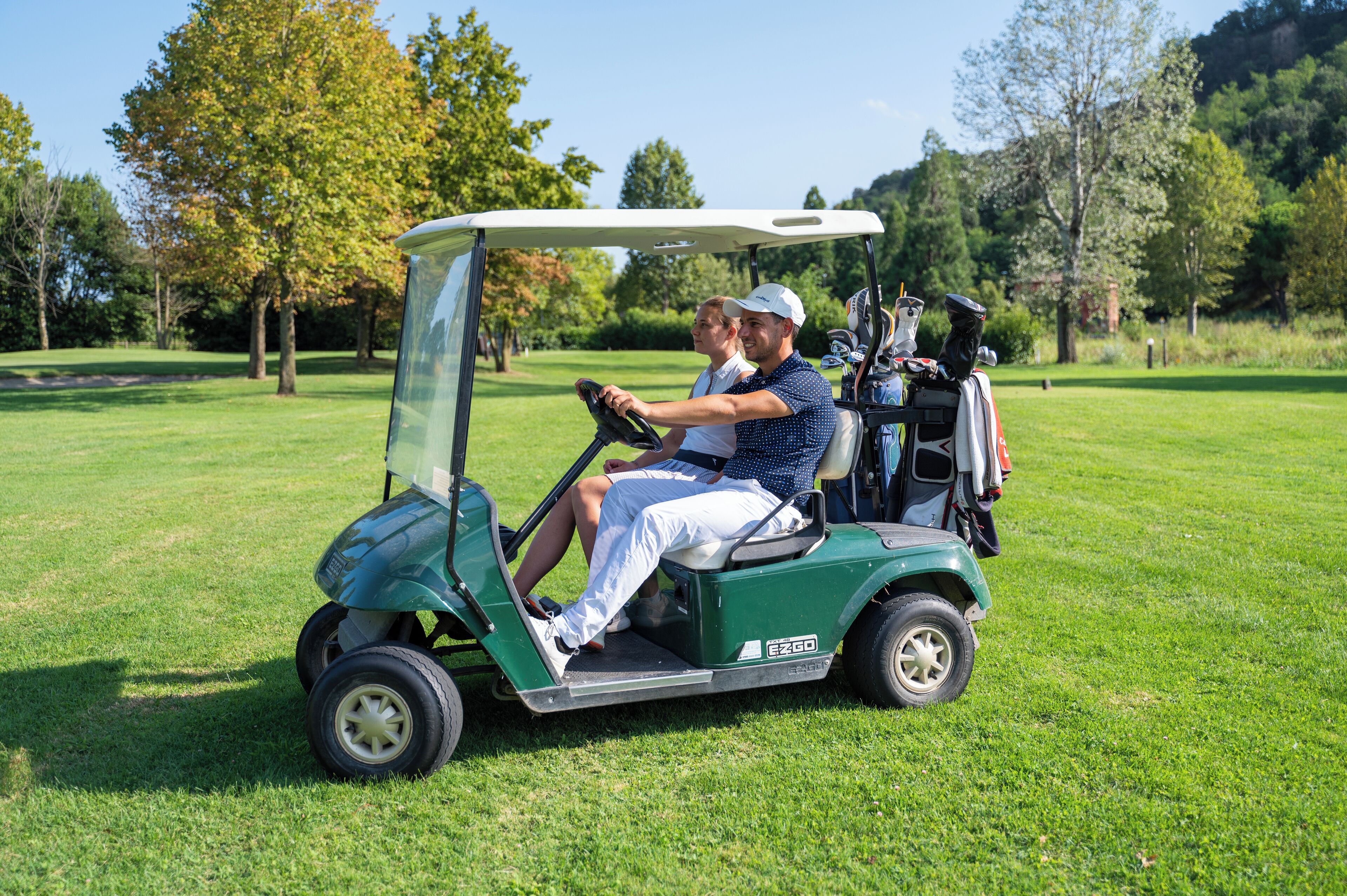 A golf cart on a green field with trees in the background.
