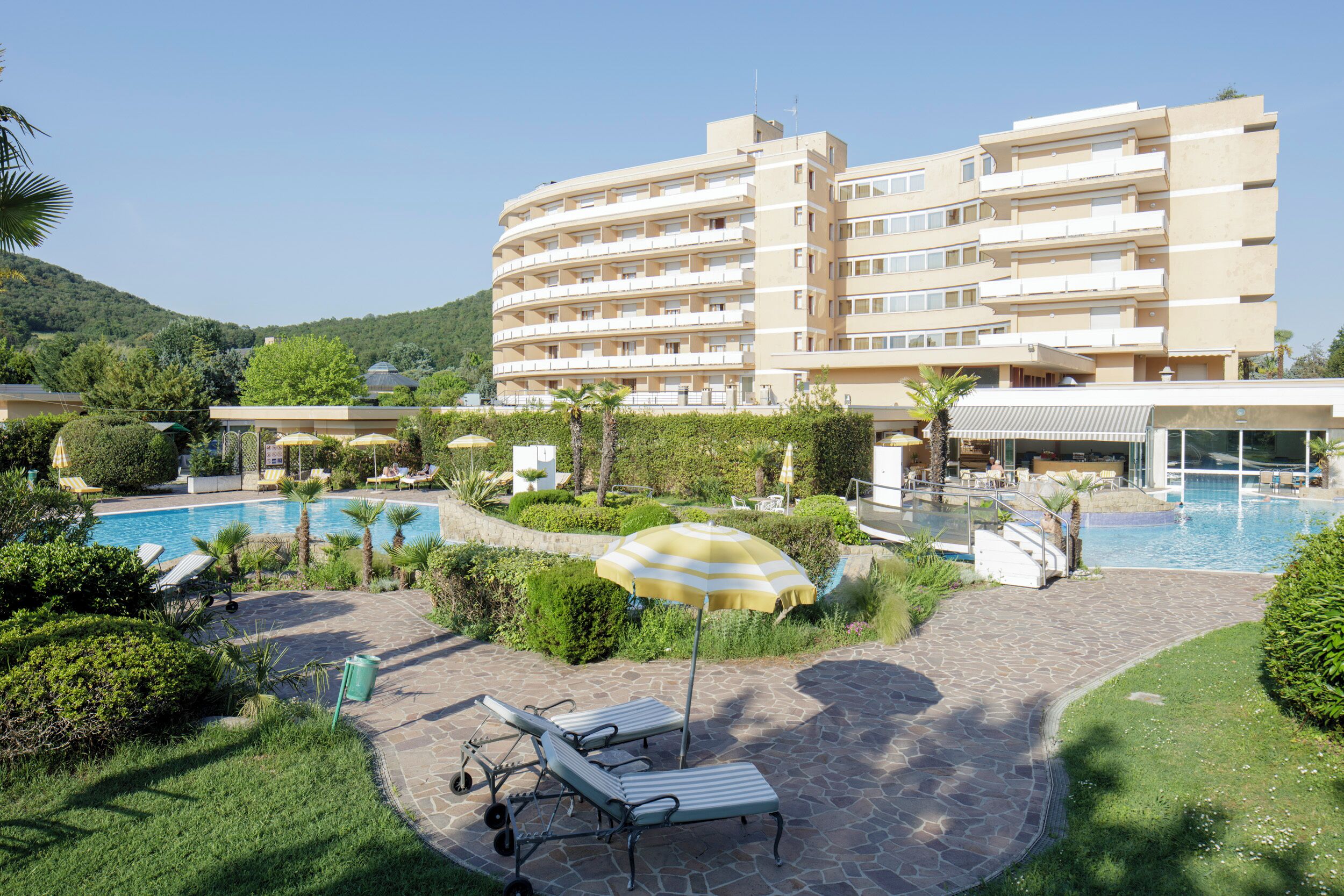 A hotel with a swimming pool, lounge chairs, and a well-maintained garden.