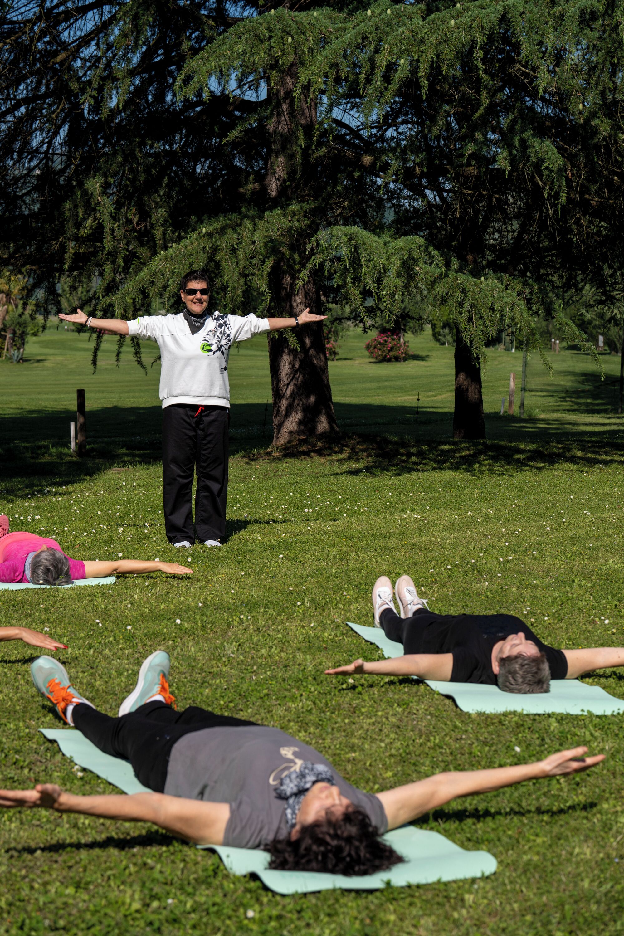 A group of people practicing yoga outdoors on a grassy area with trees in the background.
