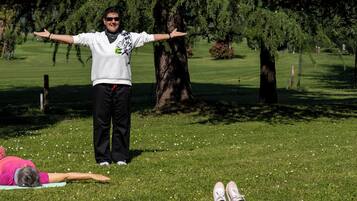 A group of people practicing yoga outdoors on a grassy area with trees in the background.