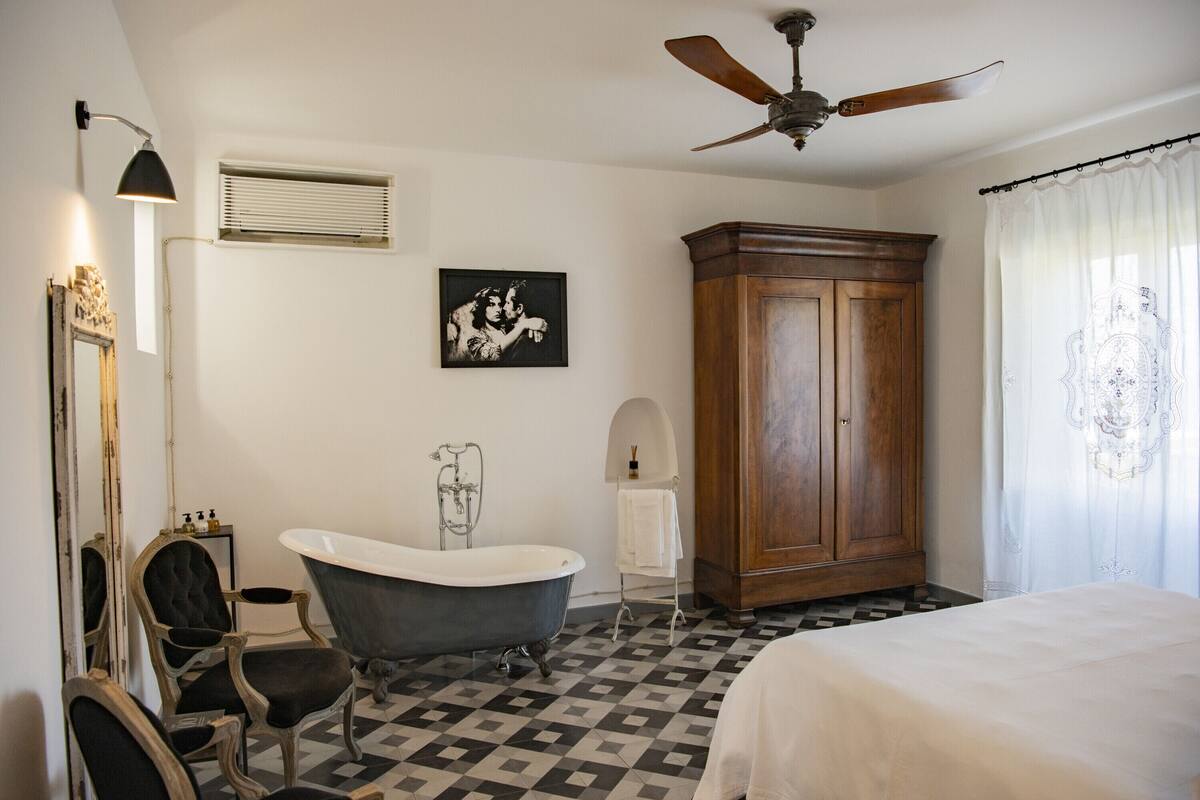 Un baño con una bañera independiente, un mueble de madera, un ventilador de techo y un espejo con marco decorativo.