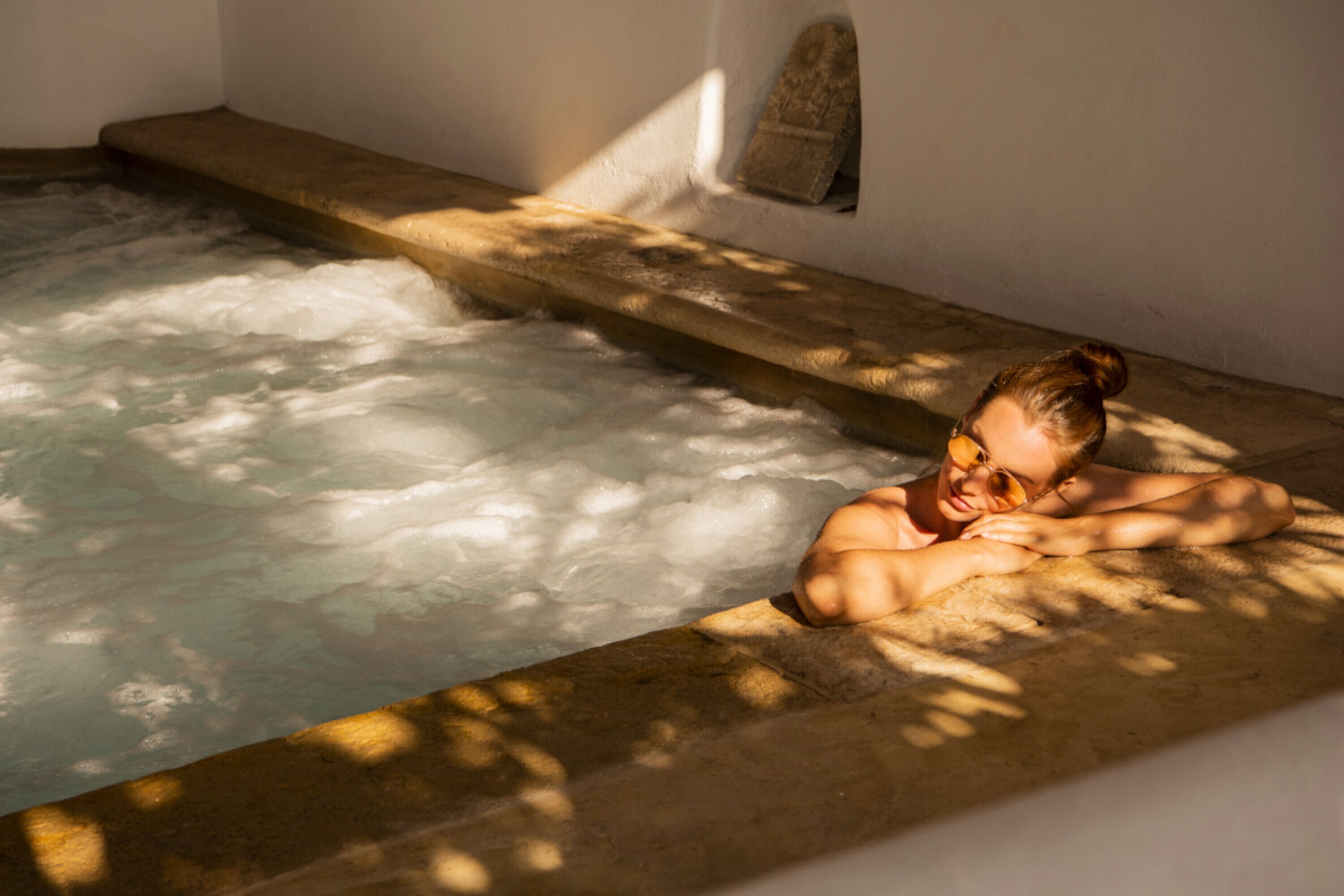 A person relaxing in a hot tub with a stone ledge and a small alcove with a cushion.