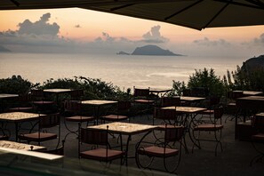 An outdoor seating area with tables and chairs, overlooking a body of water and distant land.