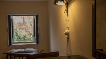 Una stanza con un tavolo, un libro aperto, una finestra con vista sul verde e una lampada fissata al muro.