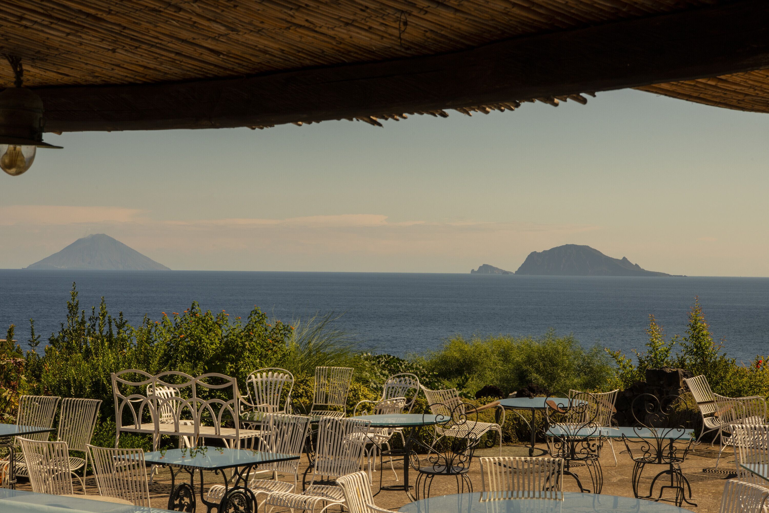 An outdoor seating area with tables and chairs, overlooking a body of water and distant islands.