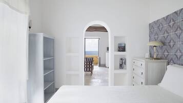 Une chambre avec un grand lit, une armoire, une commode et une vue sur la mer, visible à travers une arche.