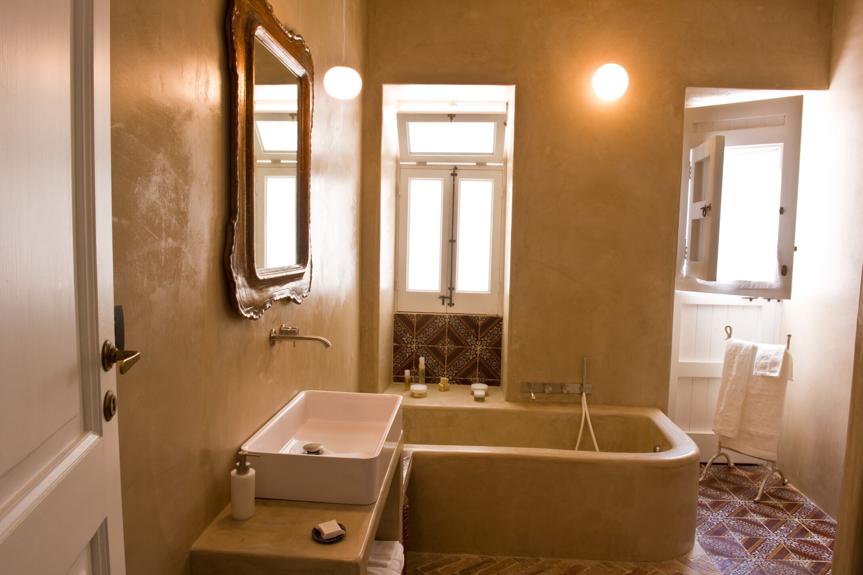 Un baño con lavamanos, bañera y espejo. Hay una ventana sobre la bañera y un perchero con toallas.