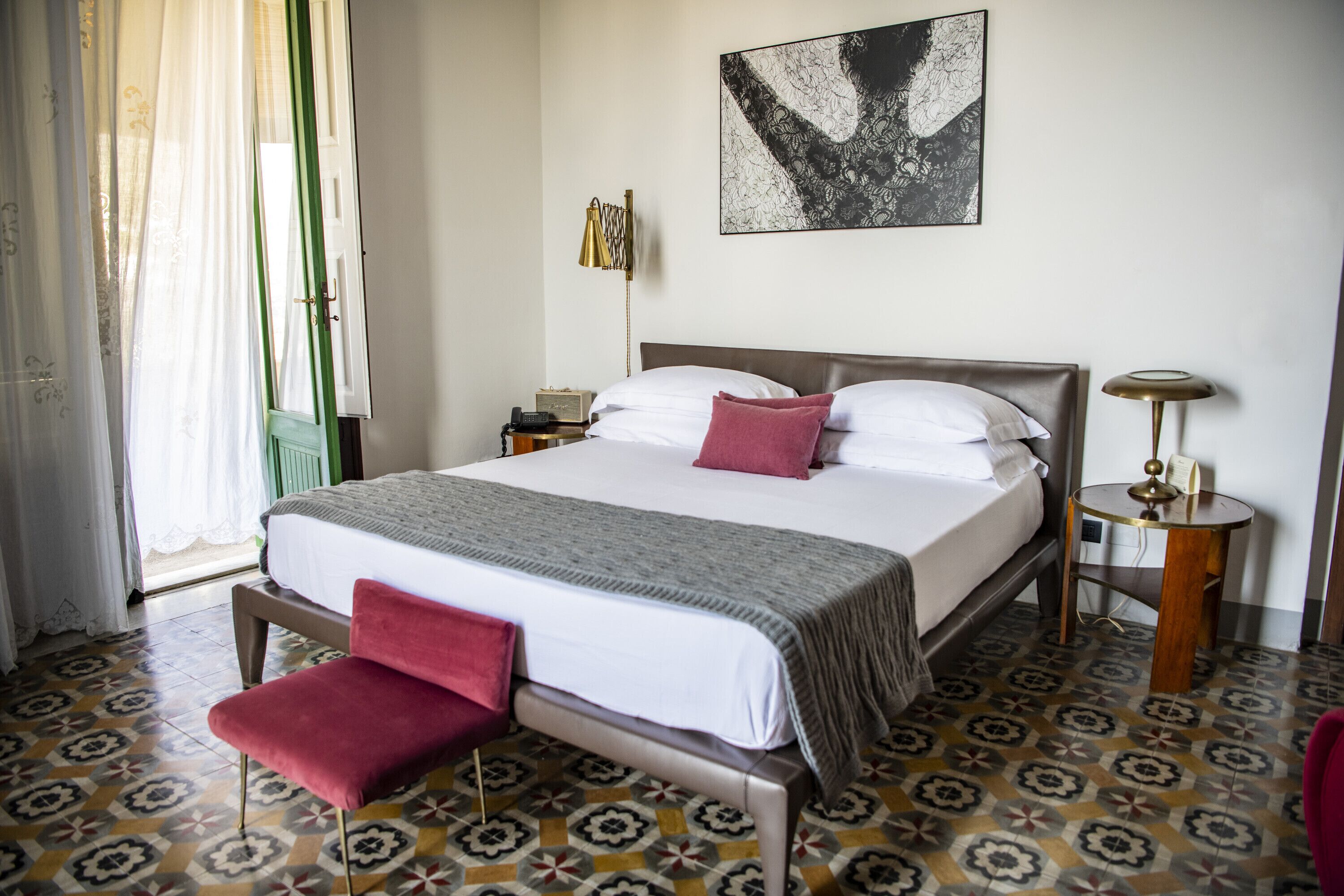 Ein ordentlich eingerichtetes Hotelzimmer mit einem großen Bett, einem Nachttisch, einer Lampe und einem gemusterten Boden.