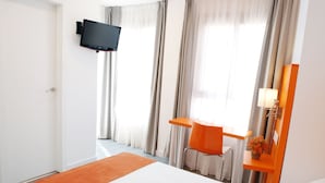 A hotel room with a bed, a desk, a chair, a TV mounted on the wall, and a window with curtains. - Hotel San Remo (Alicante)