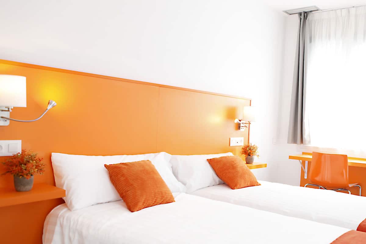 A hotel room with two beds, orange walls, white bedding, and a desk with a chair.