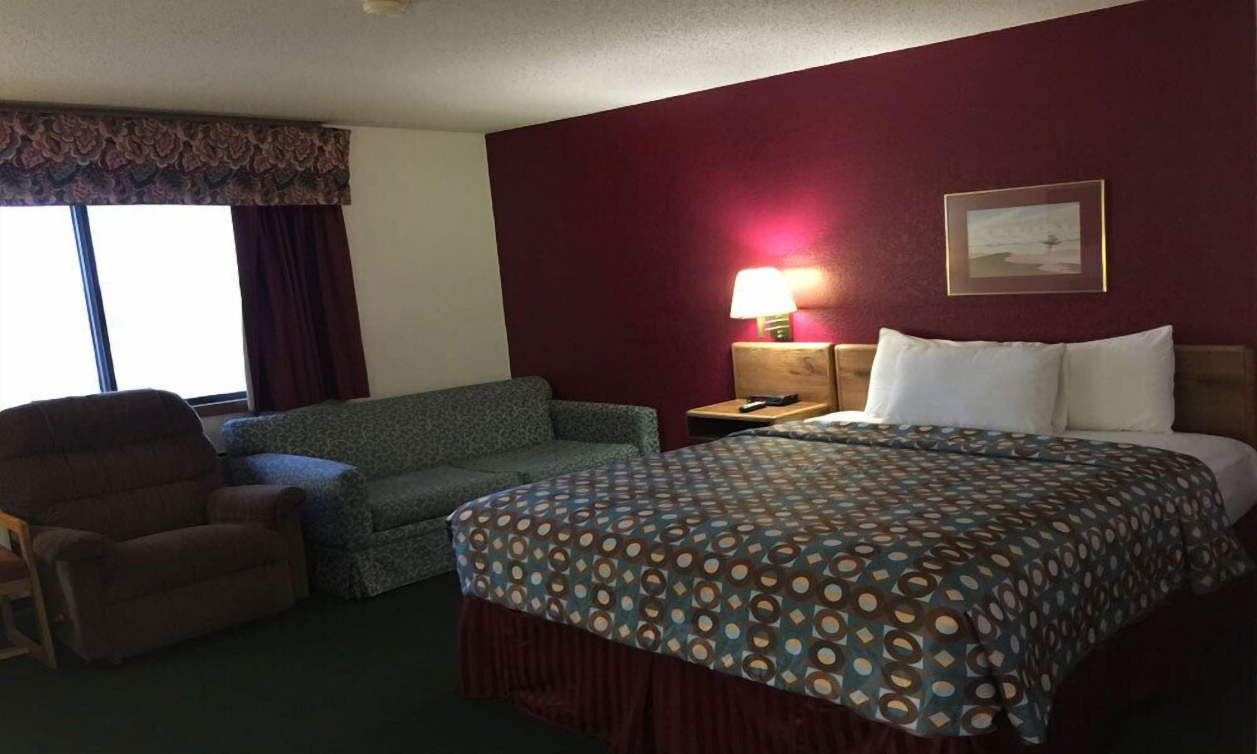 A hotel room with a bed, a sofa, a chair, a nightstand with a lamp, and a window with curtains.