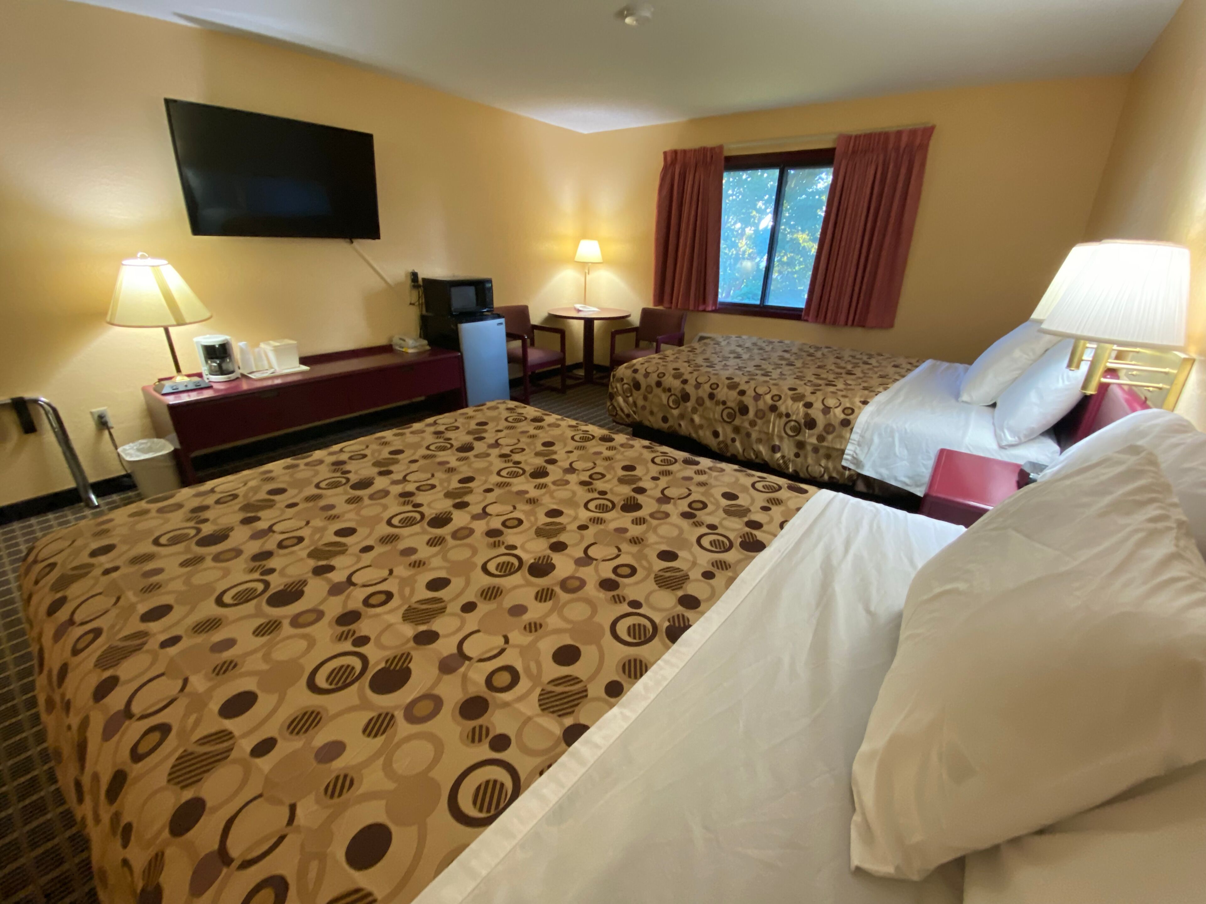 Habitación de hotel con dos camas, televisión, escritorio, silla, mesita y ventana con cortinas.