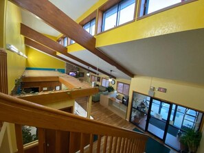 A multi-level interior with wooden beams, a staircase, and a view of the outside through large windows. - America's Stay Inn Stewartville (Stewartville)