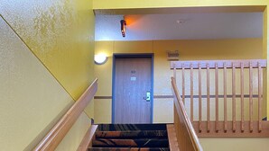 Un escalier recouvert d’une moquette à motifs et doté de rampes en bois mène à une porte portant le numéro 201.