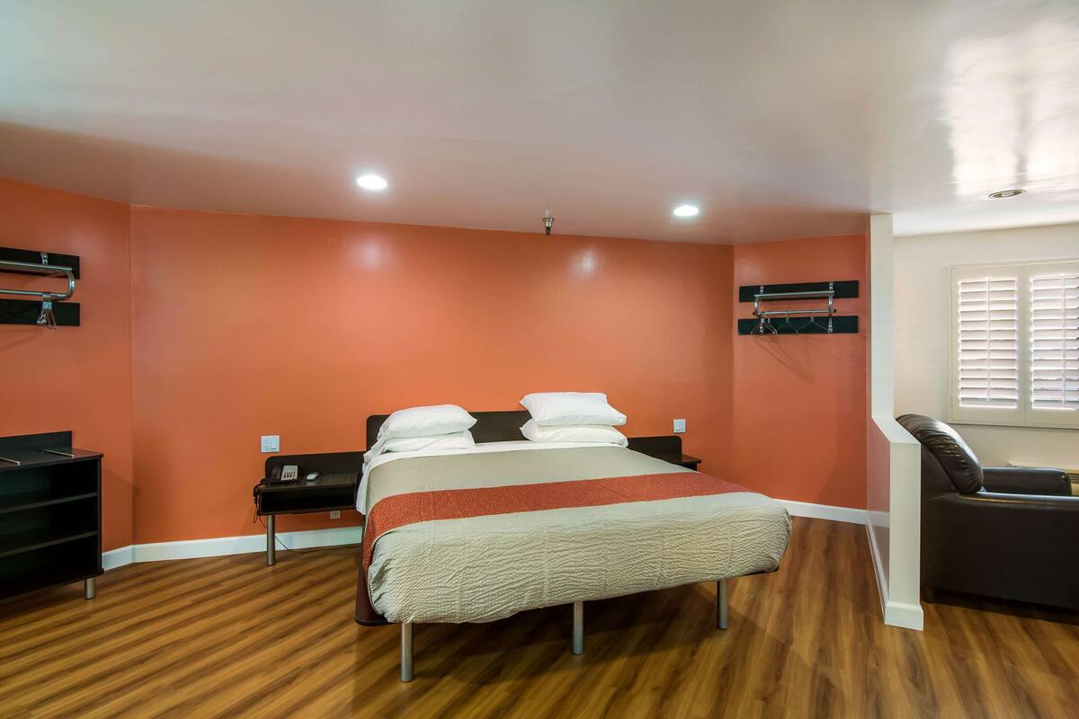 A hotel room with a bed, a nightstand, a chair, and a window with blinds.