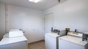 Un lavadero con dos lavadoras y una secadora, piso de baldosas y una puerta blanca.