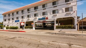 Un motel de dos pisos con techo de tejas, entrada despejada y un cartel que indica que está abierto.
