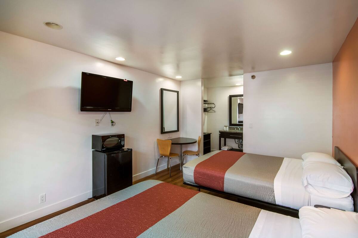 A hotel room with two beds, a TV, a desk, and a chair.