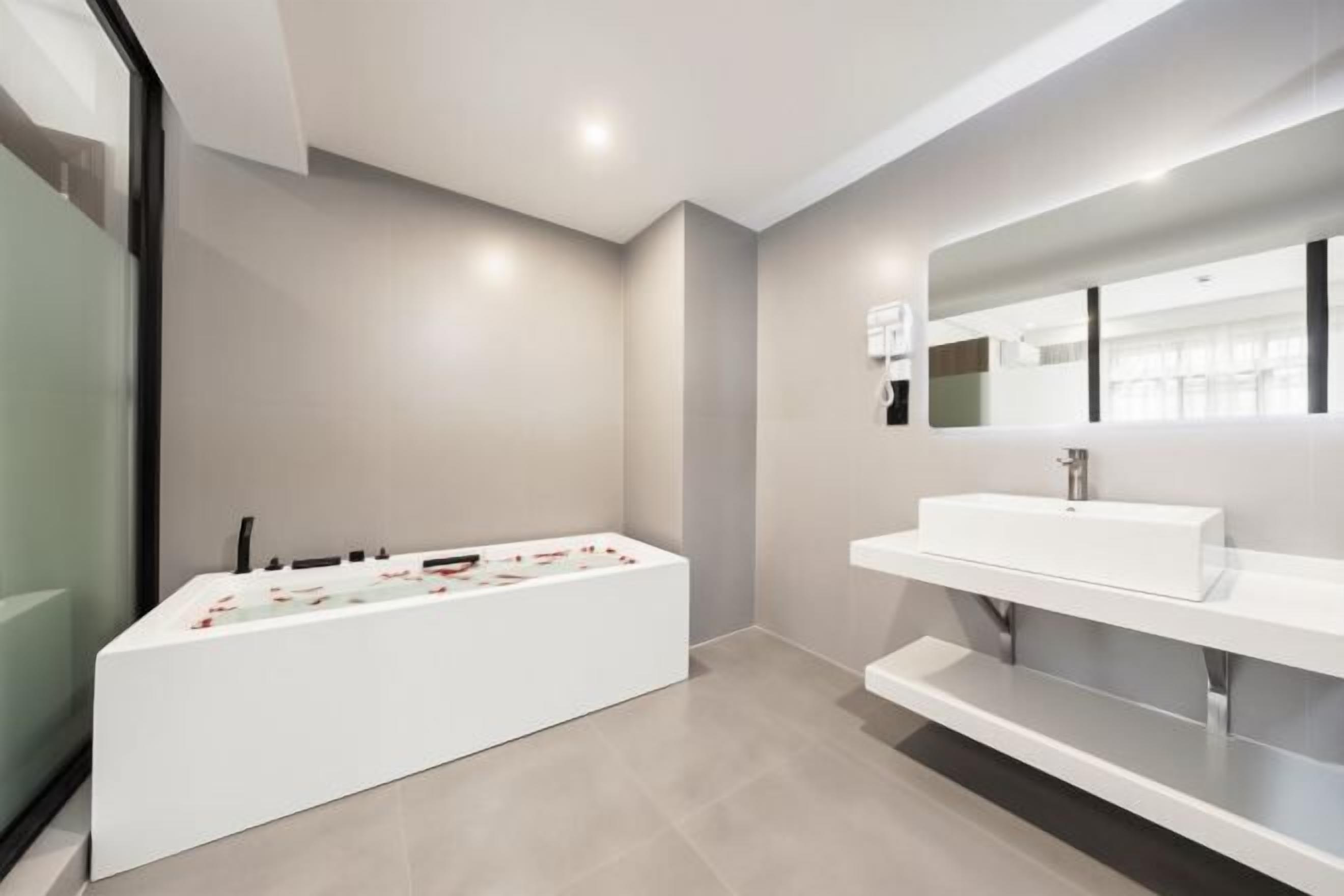 Une salle de bain moderne avec une grande baignoire, un lavabo blanc et un miroir au-dessus du lavabo.