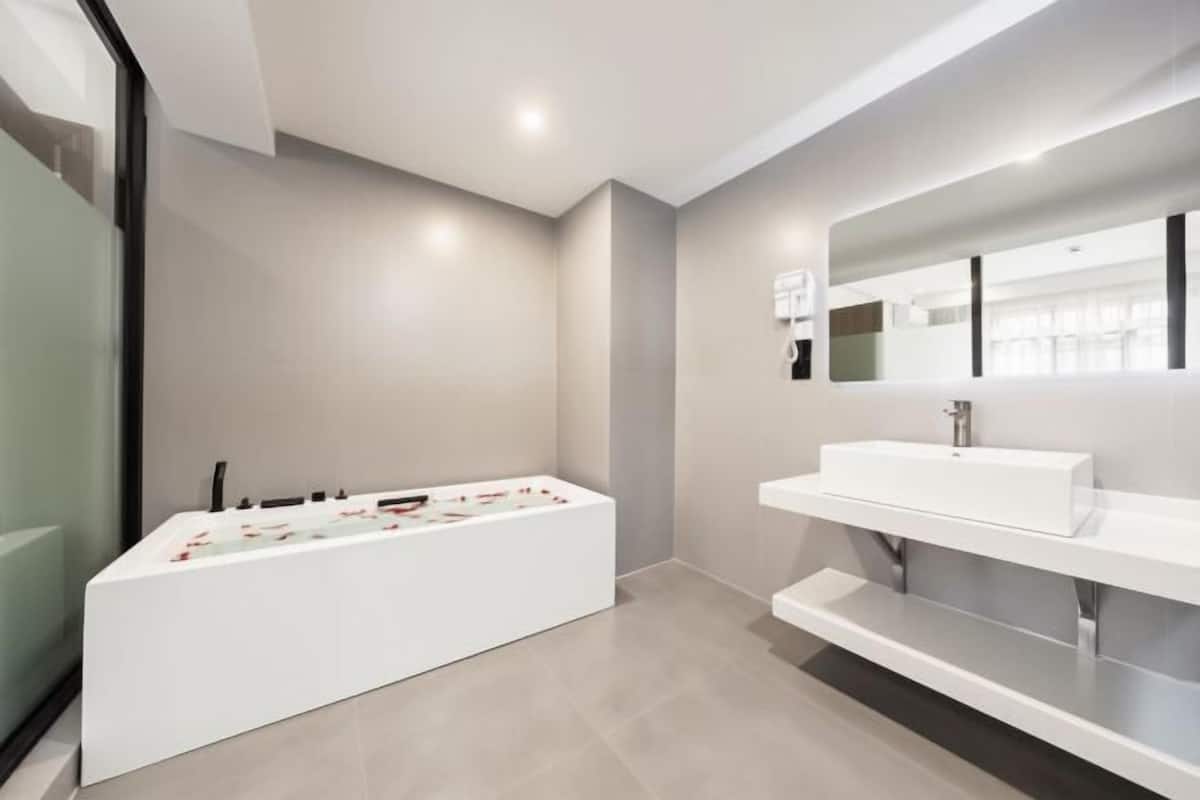 Une salle de bain moderne avec une grande baignoire, un lavabo blanc et un miroir au-dessus du lavabo.
