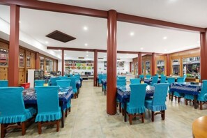 Un restaurante con techos altos, pilares de madera y sillas azules. Las mesas están preparadas con manteles blancos.
