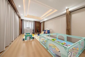 Una habitación con área de juegos, una ventana con cortinas y piso de madera.