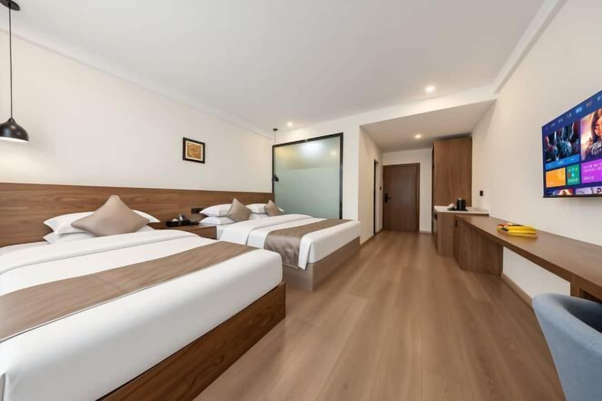 Habitación de hotel con dos camas, un escritorio, una silla y un televisor en la pared.