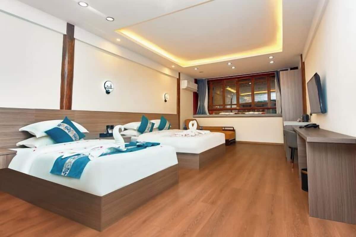 Habitación de hotel con dos camas, un escritorio, una ventana con cortinas y un diseño moderno en el techo.