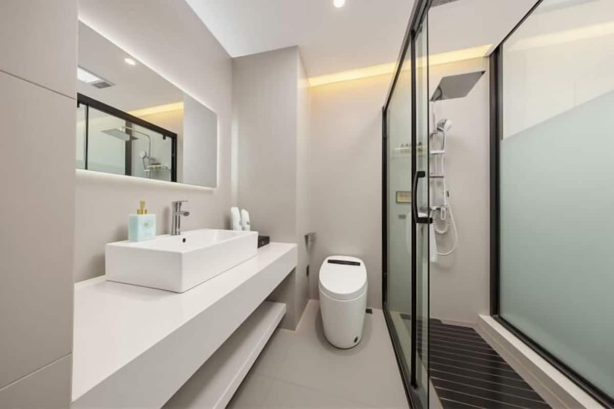 Un baño moderno con cabina de ducha de vidrio, un lavabo blanco y un espejo grande.