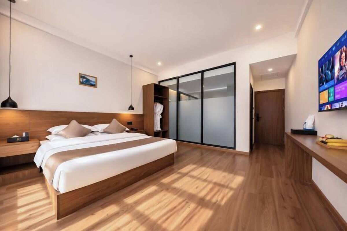 Una habitación de hotel moderna con una cama grande, cabecera de madera, televisor y armario con puerta corredera.