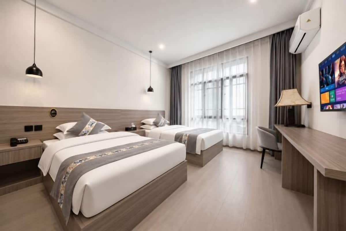 Habitación de hotel con dos camas, un escritorio, una silla, un televisor y una ventana con cortinas.