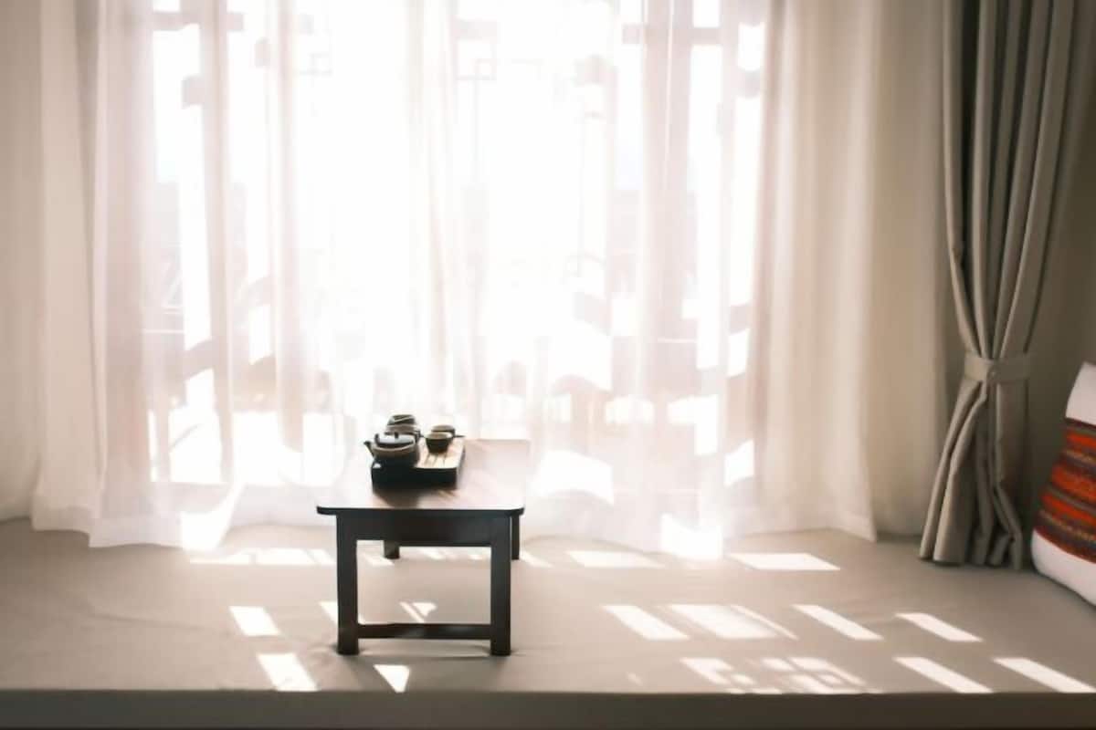 Una habitación con una cama, una mesita de noche con lámpara y cortinas translúcidas que dejan entrar luz natural.