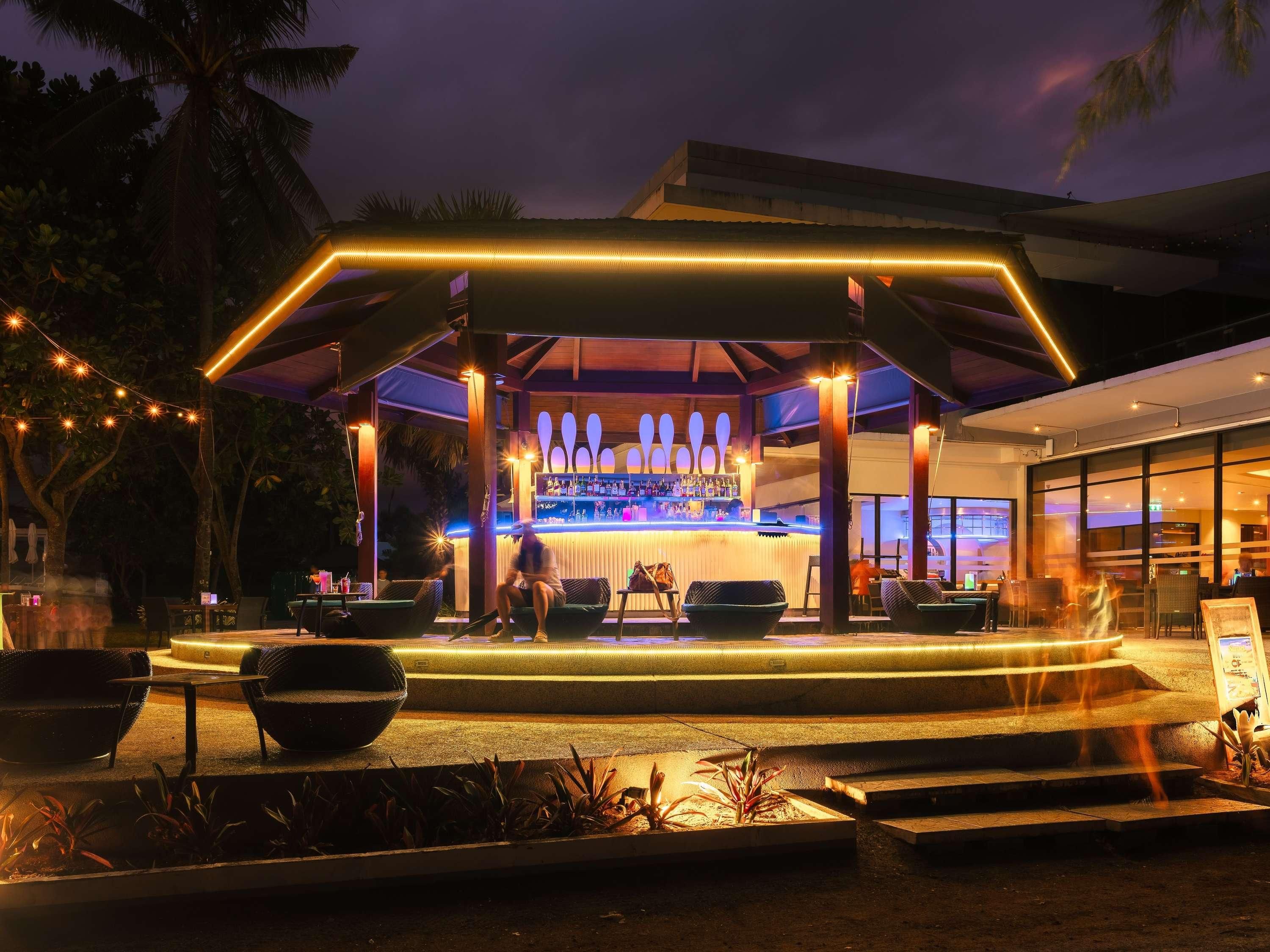 An outdoor bar area with a covered seating arrangement, a bar counter, and a pool.