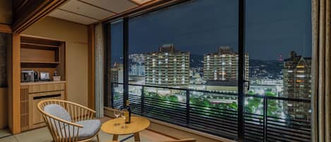 A balcony with tatami mats, a wooden chair, a small table, and a view of city buildings at night.