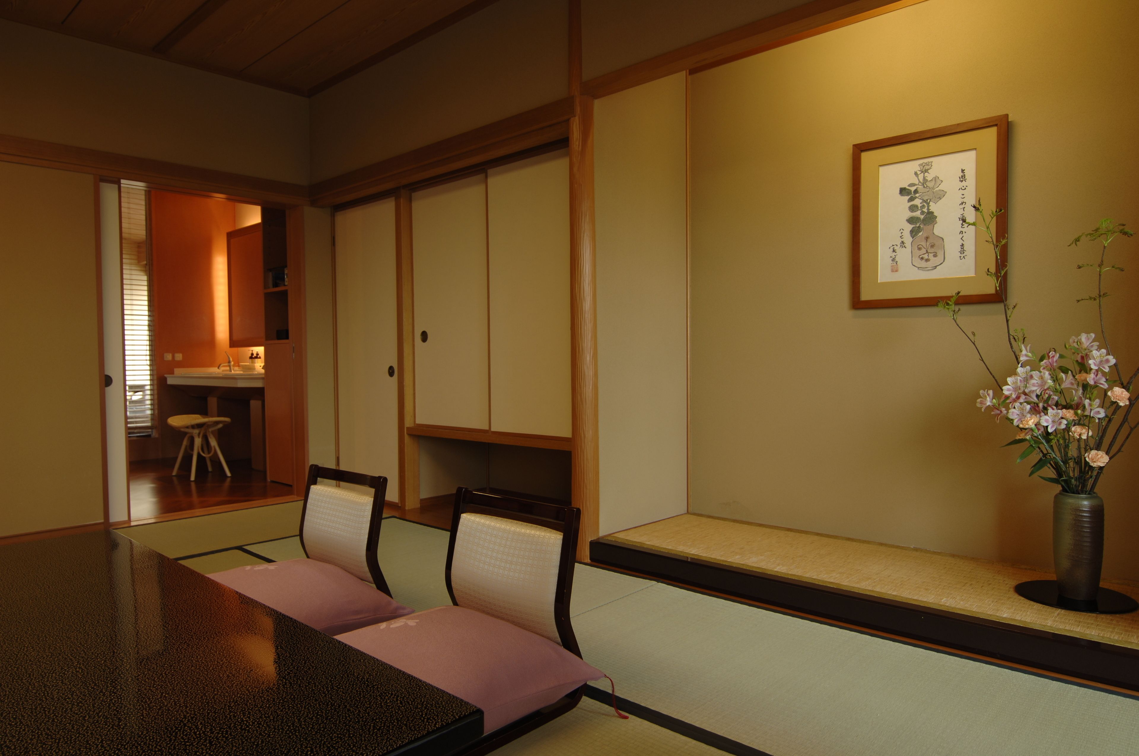 Una habitación japonesa tradicional con suelo de tatami, una mesa baja con cojines y un jarrón con flores.