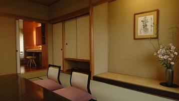Una habitación japonesa tradicional con suelo de tatami, una mesa baja con cojines y un jarrón con flores.