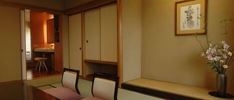A traditional Japanese room with tatami flooring, a low table with cushions, and a vase of flowers.