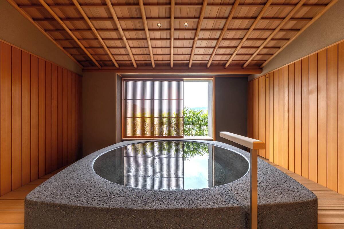 A spa room with a stone hot tub, wooden walls, and a window with bamboo blinds.