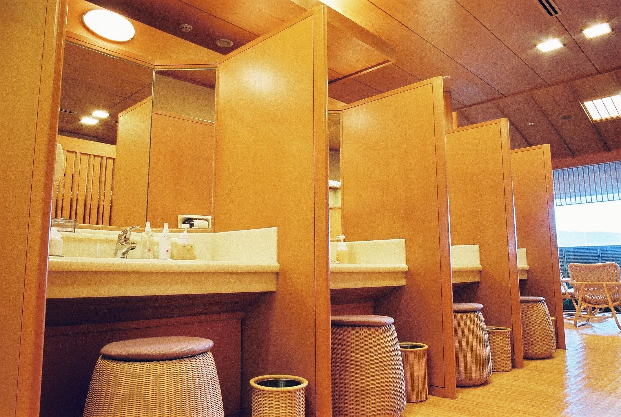 A row of wooden partitions with sinks and stools in a bathroom setting.