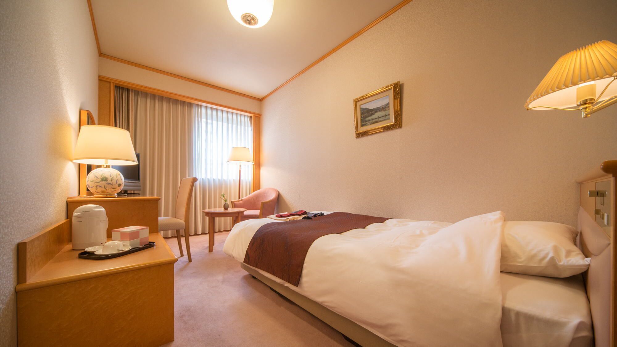 Ein Hotelzimmer mit Bett, Nachttischen, Schreibtisch, Stuhl, Lampe und einem Bild an der Wand.