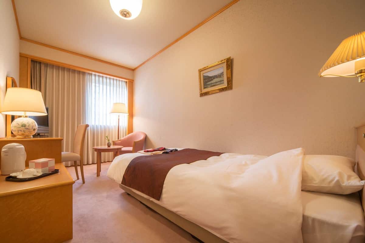 A hotel room with a bed, bedside tables, a desk, a chair, a lamp, and a picture on the wall.