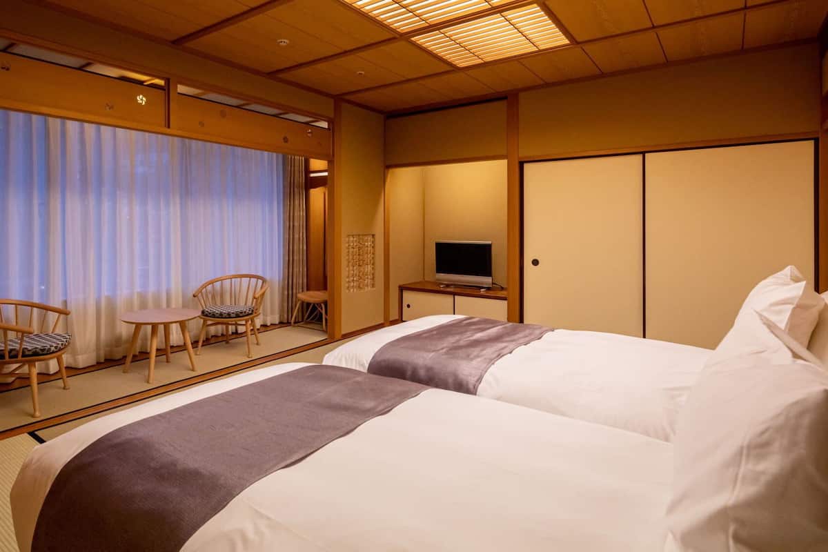 A hotel room with two beds, a TV, a small table, and chairs.