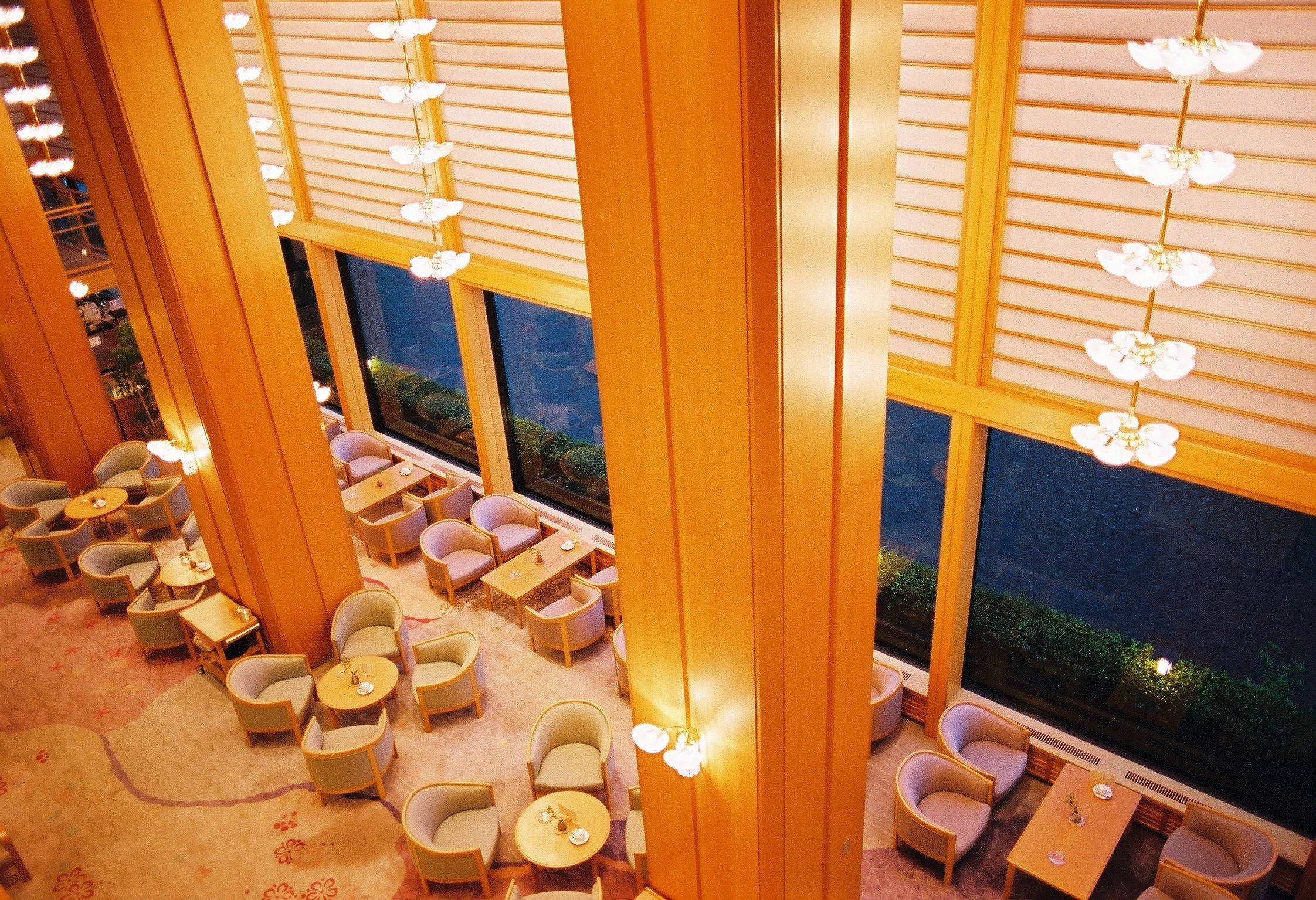 Un hall d’hôtel doté de plusieurs espaces salon, de grandes fenêtres et de luminaires suspendus.