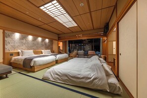 A traditional Japanese-style hotel room with tatami flooring, two beds, a view of the city at night, and a sliding door. - Hotel Wakamizu (Takarazuka)