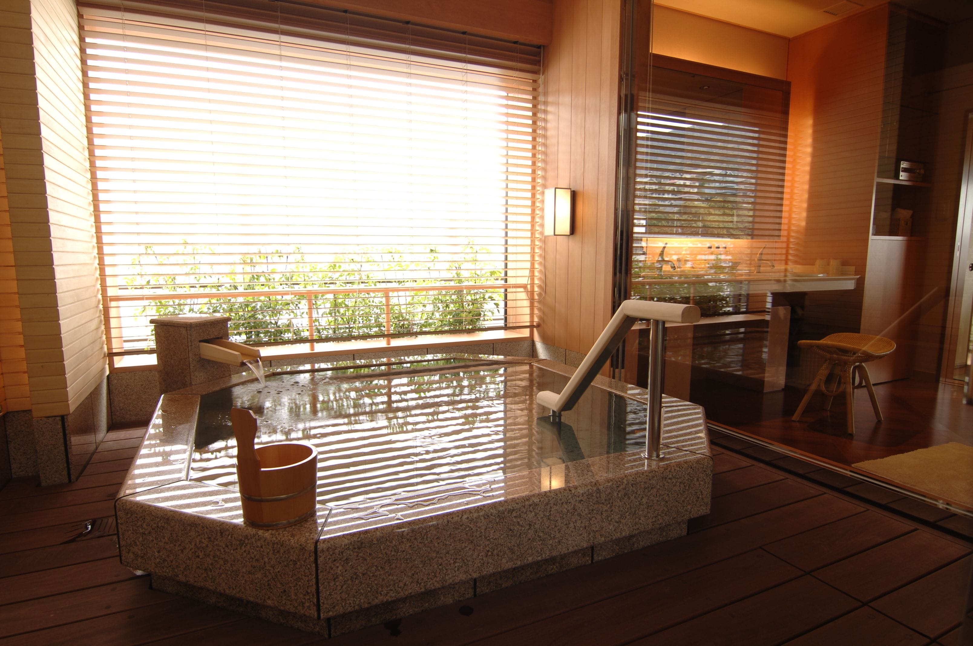 Een jacuzzi met glazen ombouw, houten vloer en uitzicht op groen.