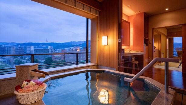 A hot tub with a view of a cityscape, a wooden bench, and a basket of flowers. - Hotel Wakamizu (Takarazuka)